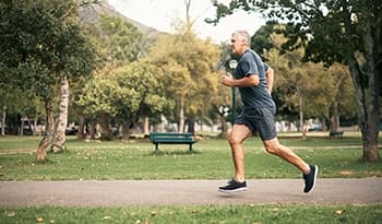 Healthy senior man running through green park 