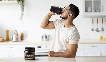 Athletic male drinking creatine protein shake in kitchen