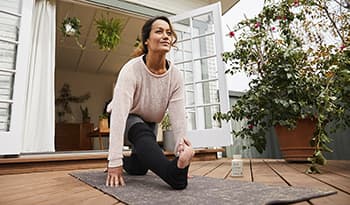 Woman stretching doing yoga on wooden deck in backyard surrounded by green plants