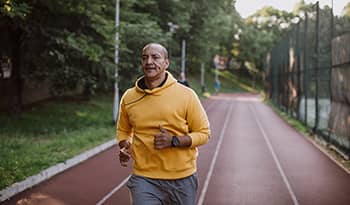 Man in yellow sweatshirt jogging outside on a track
