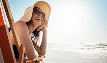 woman on the beach wearing a large sun hat and sunglasses enjoying her vacation