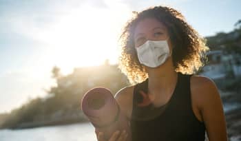 woman wearing a mask and carrying yoga mat about to practice self-care