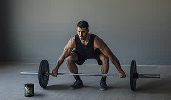 Male athlete lifting barbell with pre-workout supplement on floor