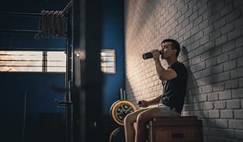Asian male taking break from workout drinking water in gym