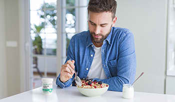 Man eating cereal and yogurt in kitchen with probiotics on table