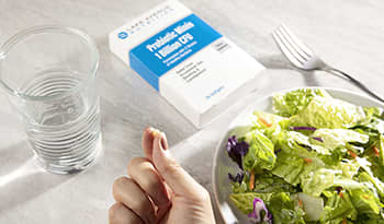 Probiotics on white marble table with salad and glass of water