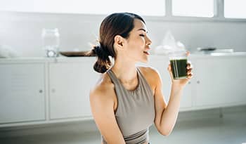 Fit Asian woman resting and having green smoothie after exercising at home