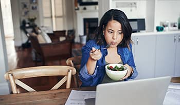 Young woman working at kitchen table eating a salad for lunch