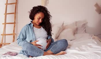 woman sitting on bed caressing pregnant belly with no stretch marks