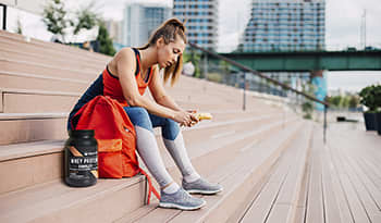 Athletic woman taking break from workout on steps with banana and protein powder