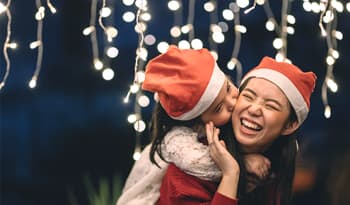 mom practicing self care by giving daughter piggy back ride wearing santa hats with holiday lights a