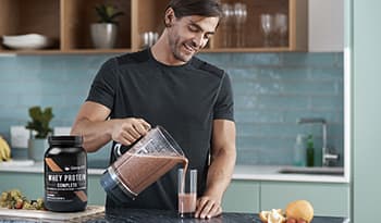 Young athletic male making protein shake in kitchen with whey protein