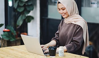 Young woman working on laptop in coffee shop with stress support supplement on table