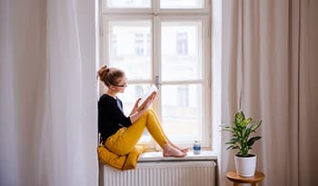 Young woman sitting in window sill reading a book