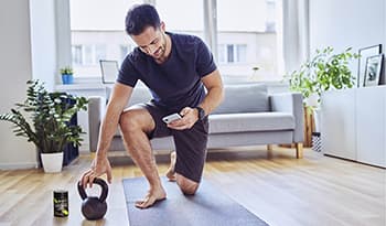 Athletic male checking phone after finishing a workout at home