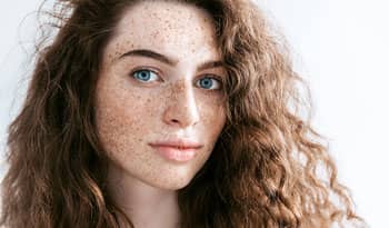 young woman with blue eyes and freckles thinking about her summer skincare routine