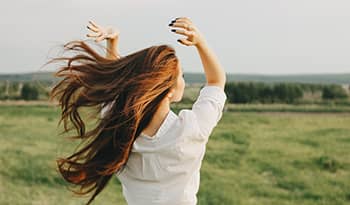 Young Asian woman with long hair standing in green field with wind blowing