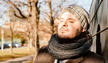 Young male with beard wearing a hat and scarf taking a deep breath 