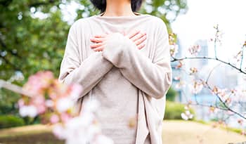 Woman surrounded by cherry blossoms with hands over heart