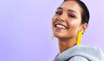 woman wearing vibrant makeup smiling in front of purple background