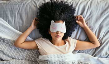 woman lying in bed with an eye mask over her eyes for self-care