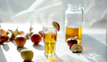 Apple cider vinegar wellness shot in glass on white background with apples and pitcher.