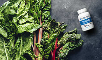 Vitamin K supplement bottle and leafy greens on concrete table