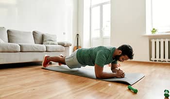 Male exercising in his living room doing a plank on a workout mat