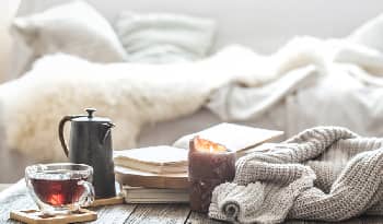 self-care items of tea, tea cup, and candle with a couch and comfortable blankets