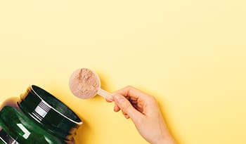 Scooping out a serving of protein powder from container on yellow background