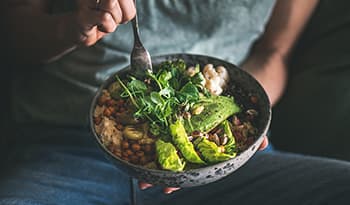 Woman in t-shirt and jeans eating vegan bowl for lunch or dinner with avocado and veggies