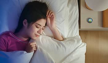 Asian woman asleep in bed with sleep balm on nightstand