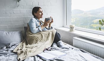 Woman drinking coffee in bed looking out the window