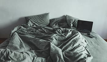 Laptop and smartphone on unmade bed with green sheets