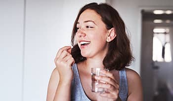 Healthy young woman with glass of water taking vitamin 