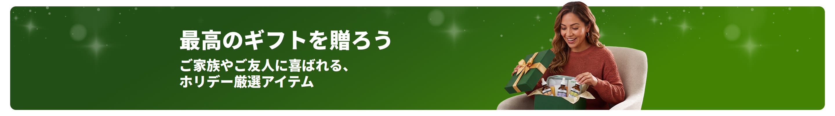 最高のギフトを贈ろう。ご家族やご友人に喜ばれる、ホリデーシーズンに厳選されたおすすめアイテム。ギフトボックスを開けて笑顔を見せる女性。