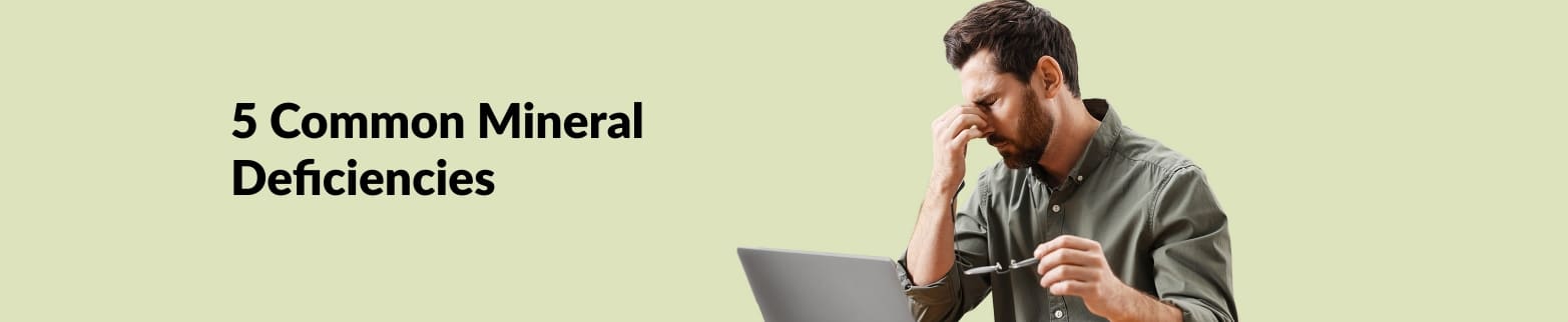 Banner for article on 5 common mineral deficiencies, featuring a fatigued man holding glasses in front of a laptop.