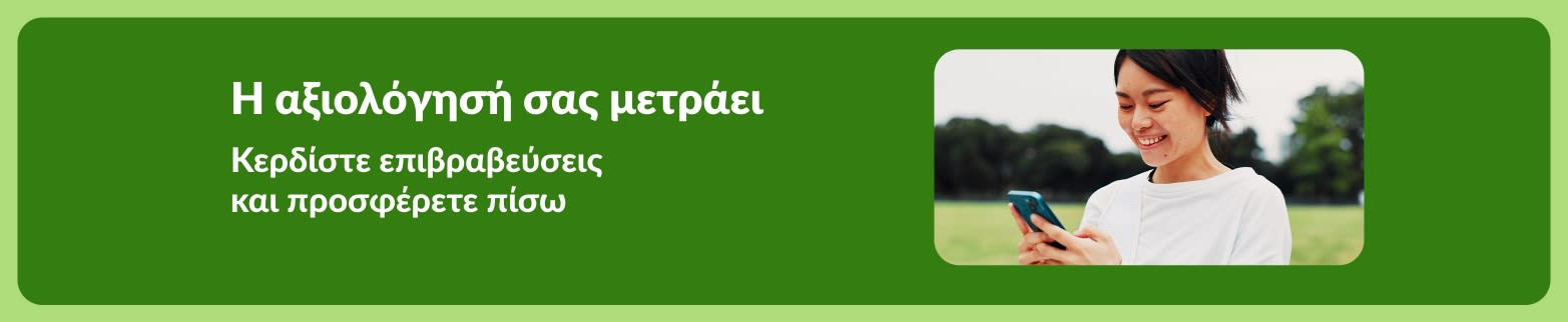 Μπάνερ της iHerb που ενθαρρύνει τους πελάτες να αφήσουν αξιολογήσεις, με μια χαμογελαστή πελάτισσα που χρησιμοποιεί smartphone σε εξωτερικό χώρο.